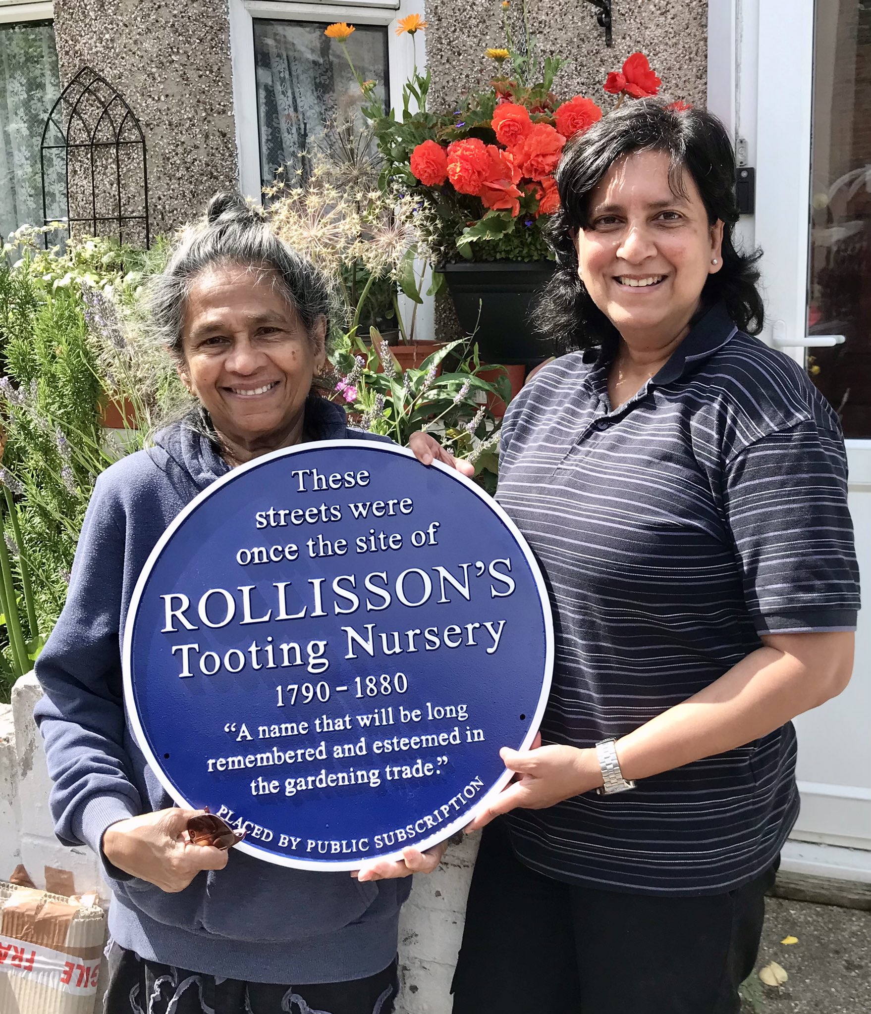 Two women holding the Rollisson's Tooting Nursery blue plaque
